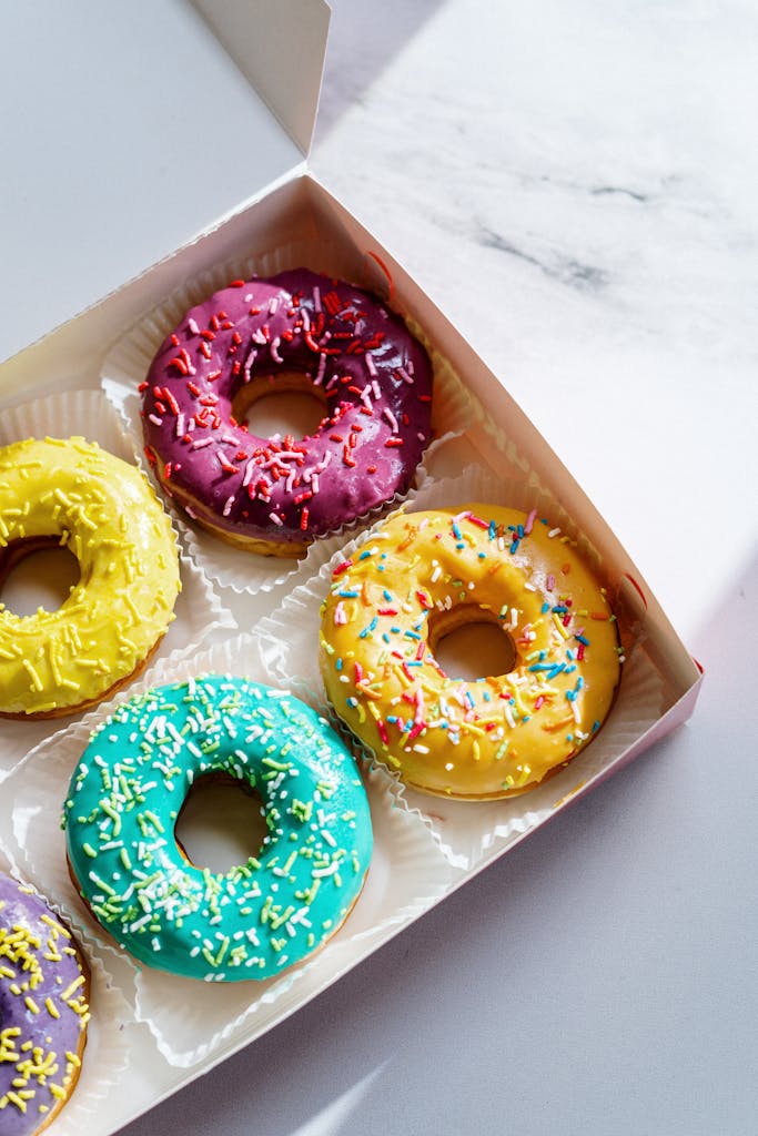 Colorful glazed donuts in a box on a marble background, perfect treat for sweet tooth.